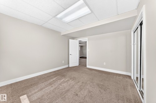 Spacious room featuring neutral paint, tan carpeting, white baseboards, and a drop ceiling with recessed lighting - 16124 76 Street, Edmonton, AB 