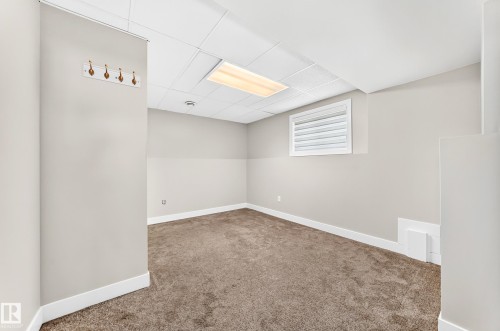 Versatile room featuring plush carpeting, light neutral wall tones, a drop ceiling with recessed lighting, and a window with white louvered blinds - 16124 76 Street, Edmonton, AB 