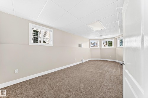 Spacious carpeted room featuring multiple windows, a drop ceiling with recessed lighting, light-toned walls, and white trim - 16124 76 Street, Edmonton, AB 