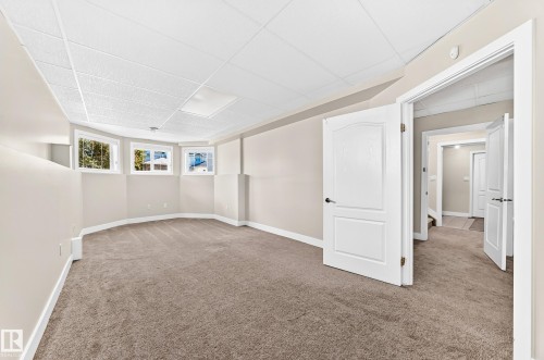 Spacious carpeted room featuring a drop ceiling with recessed lighting - 16124 76 Street, Edmonton, AB 