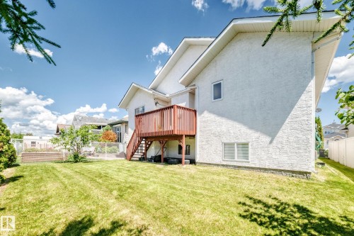 Expansive rear yard featuring a large wooden deck with stairs, white stucco exterior, and a manicured lawn - 16124 76 Street, Edmonton, AB 