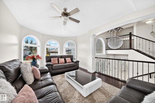 Living area featuring an open-concept design, a contemporary tiered chandelier, and a dark wood-finish staircase with wrought iron balusters - 16124 76 Street, Edmonton, AB 