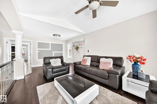 Spacious living area featuring vaulted ceilings, dark wood-finish flooring, a decorative accent wall, a ceiling fan, and built-in shelving - 16124 76 Street, Edmonton, AB 