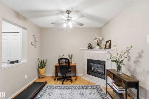 Living space featuring a corner fireplace with a tiled surround, wood-finish flooring, a ceiling fan with integrated lighting, and a partial wall opening - 3117 32 Avenue, Edmonton, AB 