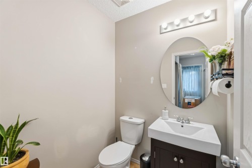 Compact bathroom featuring a contemporary dark wood-finish vanity with an integrated white sink, a chrome two-handle faucet, and an oval wall mirror with overhead bar lighting - 3117 32 Avenue, Edmonton, AB 