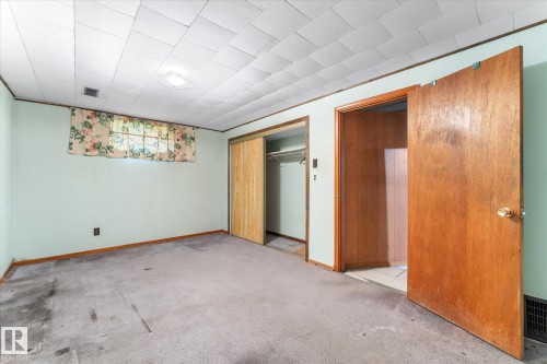 Room featuring soft green walls, wood trim, wall-mounted light fixture, and a window with floral curtains - 9315 86 Street, Edmonton, AB 