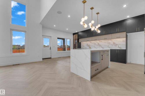 Modern kitchen featuring a waterfall island, two-tone cabinetry with under-cabinet lighting, and a marble-patterned backsplash - 7677 Kimiwan Crescent, Edmonton, AB 