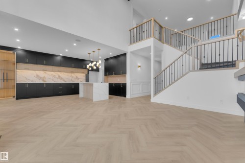 Open-concept living area featuring light wood-finish herringbone flooring, a two-story staircase with dark balusters and light wood handrails, and a contemporary kitchen - 7677 Kimiwan Crescent, Edmonton, AB 