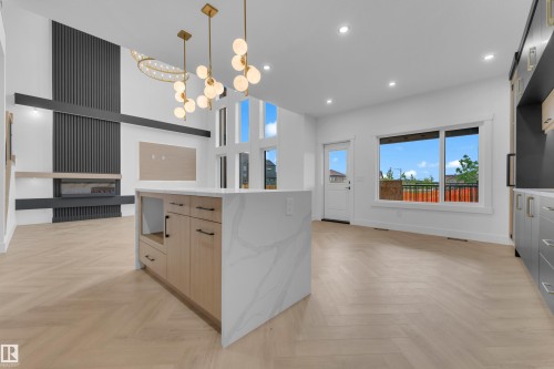 Spacious living area featuring a central kitchen island with a waterfall countertop, herringbone wood-finish flooring, a contemporary fireplace with a slatted accent wall, tall windows, and modern pendant lighting fixtures - 7677 Kimiwan Crescent, Edmonton, AB 