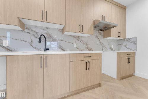 Contemporary kitchen featuring light wood-finish cabinetry with matte black hardware, white countertops, and a marble-patterned backsplash - 7677 Kimiwan Crescent, Edmonton, AB 