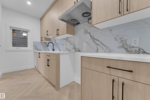 Contemporary kitchen area featuring light wood-finish cabinetry with matte black hardware, white countertops, and a full-height stone-look backsplash - 7677 Kimiwan Crescent, Edmonton, AB 