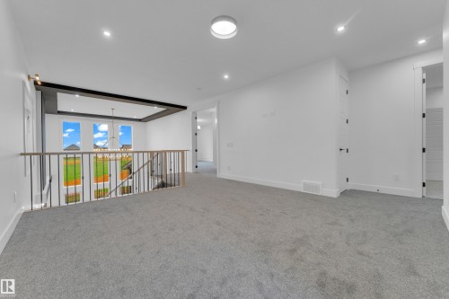 Upper-level landing featuring light gray carpeting, white walls, and a contemporary metal and wood railing overlooking a lower-level space with multiple windows - 7677 Kimiwan Crescent, Edmonton, AB 
