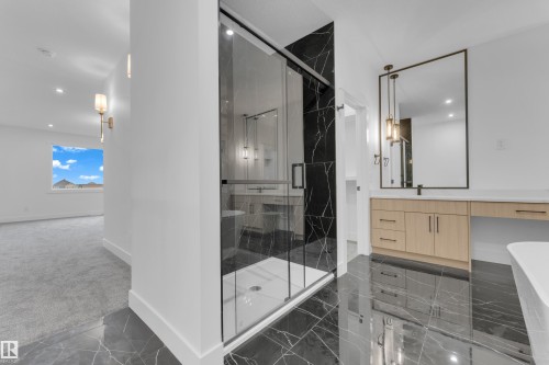 Spacious bathroom featuring a glass-enclosed shower with black-veined tile surround, a light wood-finish vanity with a white countertop and rectangular mirror, and dark polished tile flooring - 7677 Kimiwan Crescent, Edmonton, AB 