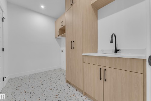 Laundry room featuring light wood-finish cabinetry with black hardware, white countertop with an undermount sink, and a black gooseneck faucet - 7677 Kimiwan Crescent, Edmonton, AB 