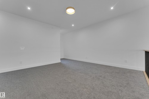 Spacious room featuring neutral carpeting, white walls, recessed lighting, and a contemporary flush-mount light fixture - 7677 Kimiwan Crescent, Edmonton, AB 