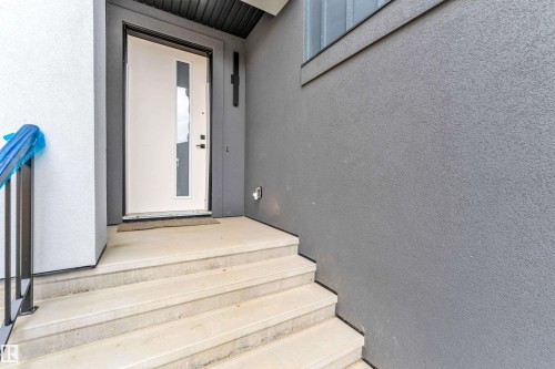 Contemporary entry featuring a white door with vertical glass panel, concrete steps, and a dark metal handrail - 7677 Kimiwan Crescent, Edmonton, AB 