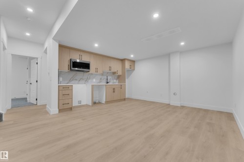Open-concept living space with light wood-finish flooring, recessed lighting, and a contemporary kitchenette featuring wood cabinetry, a built-in microwave, and a white marble-patterned backsplash - 7677 Kimiwan Crescent, Edmonton, AB 