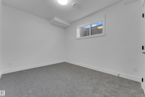 Carpeted room featuring white walls, a single window with a window well, and a flush-mount ceiling light fixture - 7677 Kimiwan Crescent, Edmonton, AB 