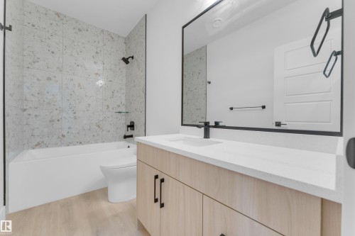 Bathroom featuring a light wood-finish vanity with a light countertop, black fixtures, a rectangular mirror, and a tiled shower/tub combination - 7677 Kimiwan Crescent, Edmonton, AB 