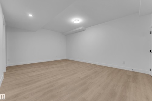 Bright interior room featuring wood-finish flooring, white baseboards, and neutral wall paint - 7677 Kimiwan Crescent, Edmonton, AB 