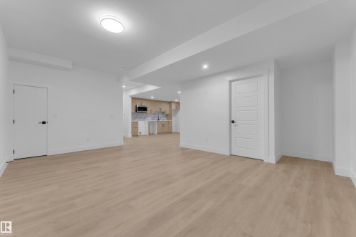 Spacious room featuring light wood-finish flooring, recessed lighting, and a modern kitchen area with light wood cabinetry and a stainless steel microwave - 7677 Kimiwan Crescent, Edmonton, AB 