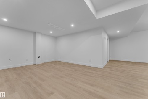 Spacious room featuring light wood-finish flooring, recessed lighting, white walls, and bright white baseboards - 7677 Kimiwan Crescent, Edmonton, AB 