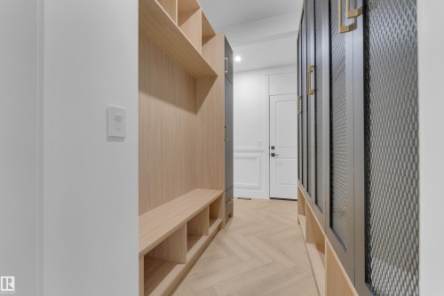 Hallway featuring herringbone wood-finish flooring, light wood-finish built-in shelving, a built-in bench, and black cabinetry with gold-tone hardware - 7677 Kimiwan Crescent, Edmonton, AB 