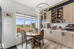 Kitchen dining area featuring a large window, light wood-finish flooring, a contemporary circular pendant light, flat-panel cabinetry with black hardware, and a tile backsplash - 