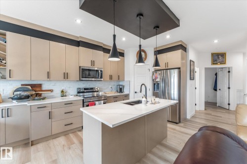 Contemporary kitchen featuring light beige cabinetry, stainless steel appliances, a white subway tile backsplash, and a central island with a white countertop and integrated sink - 94 Elm Street, Fort Saskatchewan, AB 