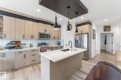 Contemporary kitchen featuring light beige cabinetry, stainless steel appliances, a white subway tile backsplash, and a central island with a white countertop and integrated sink - 