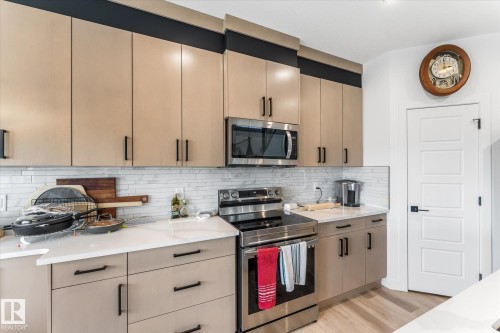 Modern kitchen featuring light-toned cabinetry with matte black hardware, stainless steel appliances, white countertops, and a subway tile backsplash - 94 Elm Street, Fort Saskatchewan, AB 