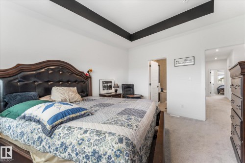 Bedroom featuring a tray ceiling with dark accents, light-toned carpet flooring, white walls, and doorway access to an additional space - 94 Elm Street, Fort Saskatchewan, AB 