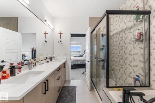 Contemporary bathroom featuring a double vanity with integrated sinks, a large mirror, modern wall-mounted lighting, and a glass-enclosed shower with patterned tile - 94 Elm Street, Fort Saskatchewan, AB 