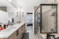 Contemporary bathroom featuring a double vanity with integrated sinks, a large mirror, modern wall-mounted lighting, and a glass-enclosed shower with patterned tile - 