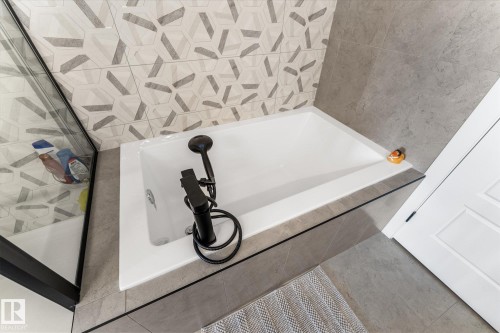 Soaking tub with matte black fixtures, set against a grey and geometric tiled wall - 94 Elm Street, Fort Saskatchewan, AB 