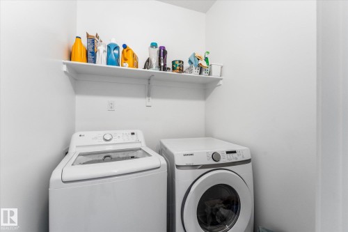 Dedicated laundry area featuring a top-load washing machine, a front-load washing machine, and a wall-mounted storage shelf - 94 Elm Street, Fort Saskatchewan, AB 