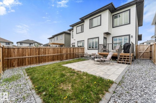 Rear exterior featuring white horizontal siding with dark trim, a wooden deck, a ground-level paver patio, a fenced yard, and a gravel border - 94 Elm Street, Fort Saskatchewan, AB 
