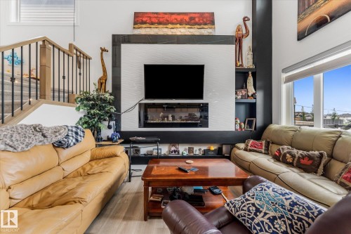 Living area featuring an integrated media wall with a linear fireplace, built-in shelving, and large picture windows - 94 Elm Street, Fort Saskatchewan, AB 