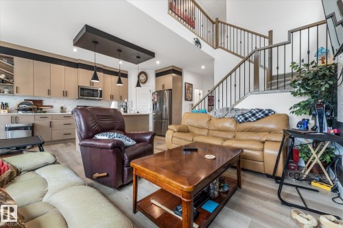 Open-concept living space featuring wood-finish flooring, a two-story staircase with metal balusters, a kitchen island, pendant lighting, and stainless steel appliances - 94 Elm Street, Fort Saskatchewan, AB 