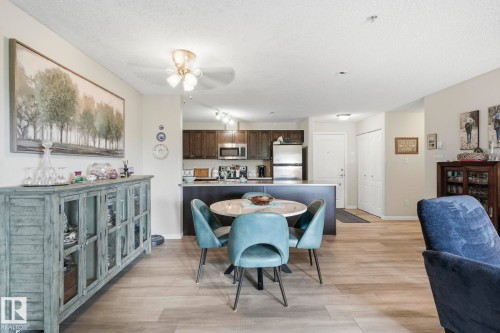 Open-concept living space featuring wood-finish flooring, a contemporary ceiling fan, and a kitchen with dark cabinetry, stainless steel appliances, and a breakfast bar - 1223 9363 Simpson Dr, Edmonton, AB 