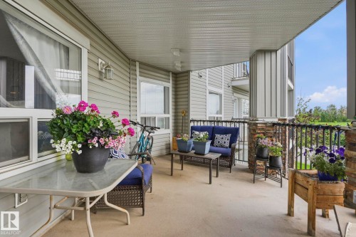 Expansive covered patio featuring a concrete floor, stone accent pillars, black wrought iron railing, and horizontal siding - 1223 9363 Simpson Dr, Edmonton, AB 