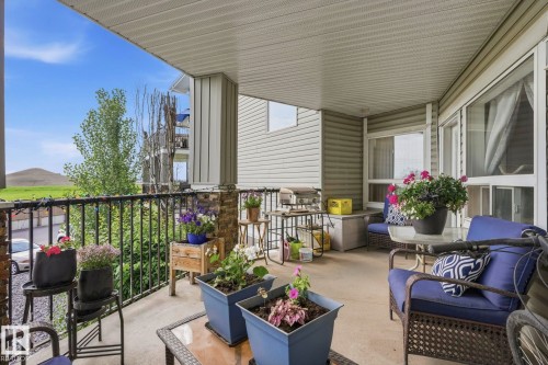 Covered outdoor patio featuring a concrete floor, black metal railings, and stone-clad support pillars - 1223 9363 Simpson Dr, Edmonton, AB 