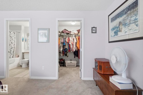 Carpeted interior space featuring a walk-in closet and access to a full bathroom with a tub/shower combination and wood-finish flooring - 1223 9363 Simpson Dr, Edmonton, AB 