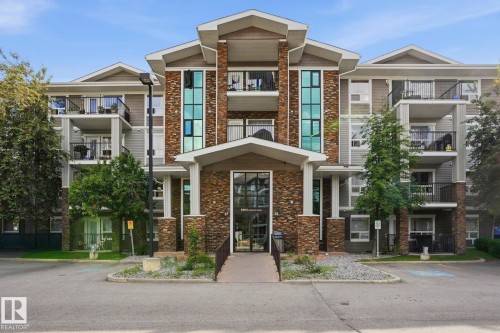 Multi-level building with stone and siding exterior, featuring multiple balconies with black railings, a central covered entrance, and mature landscaping - 1223 9363 Simpson Dr, Edmonton, AB 