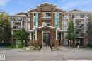 Multi-level building with stone and siding exterior, featuring multiple balconies with black railings, a central covered entrance, and mature landscaping - 1223 9363 Simpson Dr, Edmonton, AB 
