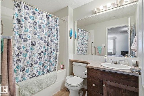 Bathroom featuring a built-in tub with shower, single vanity with a wood-finish cabinet, a large frameless mirror, and overhead vanity lighting - 1223 9363 Simpson Dr, Edmonton, AB 