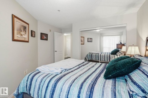 Bedroom featuring a full-wall mirrored closet, light neutral wall paint, and overhead lighting - 1223 9363 Simpson Dr, Edmonton, AB 