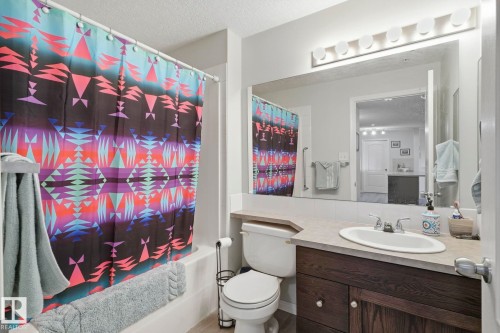 Full bathroom featuring a single vanity with a dark wood-finish cabinet, light countertop, and a large mirror with overhead lighting - 1223 9363 Simpson Dr, Edmonton, AB 