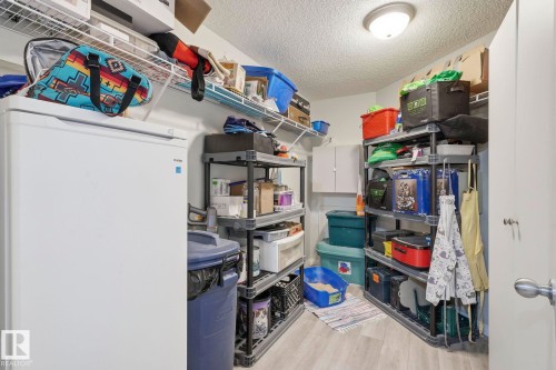Utility space featuring light wood-finish flooring, ample wall-mounted shelving, overhead lighting, and a freestanding refrigerator - 1223 9363 Simpson Dr, Edmonton, AB 