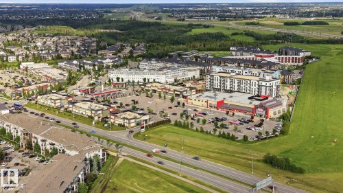 Aerial perspective showcasing a mixed-use development with residential buildings, commercial establishments, and ample surface parking - 1223 9363 Simpson Dr, Edmonton, AB 